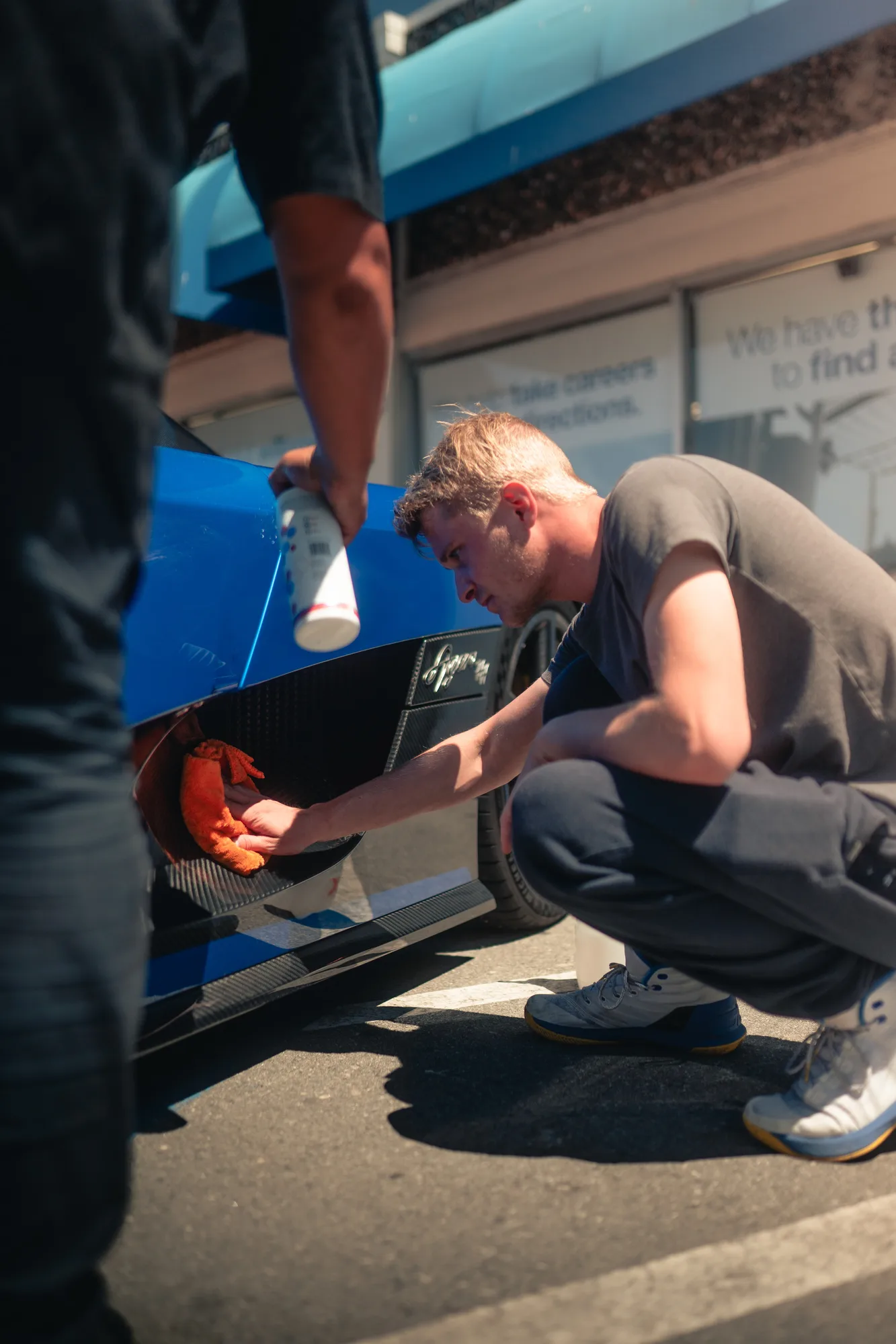 A detailer working carefully on a blue vehicle panel